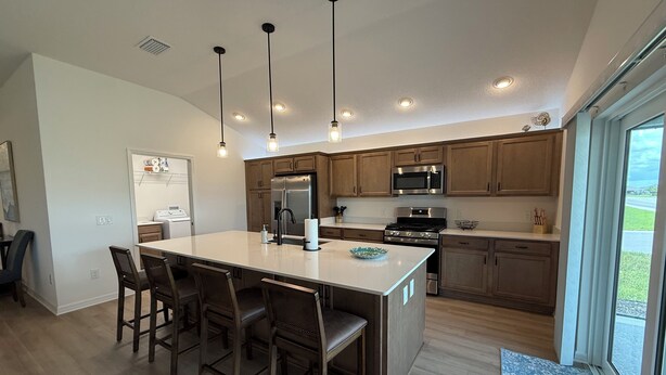 Una cocina moderna con una isla central, armarios de madera, electrodomésticos de acero inoxidable e iluminación colgante.
