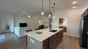 Una cocina moderna con una isla central, iluminación colgante y lavavajillas integrado.