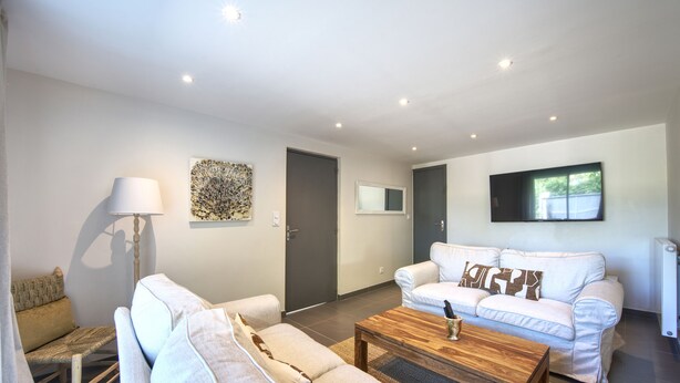 A modern living room with a sofa set, a coffee table, a floor lamp, and a flat-screen TV mounted on the wall. - L'Oustal Occitan: Idyllic Family Escape with Private Pool (Saint-Privat-des-Vieux)