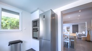 A modern kitchen with a stainless steel refrigerator, microwave, and oven, a trash bin, and a dining area with a table and chairs. - L'Oustal Occitan: Idyllic Family Escape with Private Pool (Saint-Privat-des-Vieux)