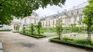 A courtyard with a paved area, benches, and greenery. - PARISIAN LIVING IN LE MARAIS: SPACIOUS FAMILY APARTMENT WITH GARDEN VIEW - 3 BED (Paris)
