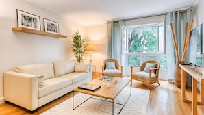 A modern living room with a sofa, two armchairs, a coffee table, and a large window with curtains. - PARISIAN LIVING IN LE MARAIS: SPACIOUS FAMILY APARTMENT WITH GARDEN VIEW - 3 BED (Paris)