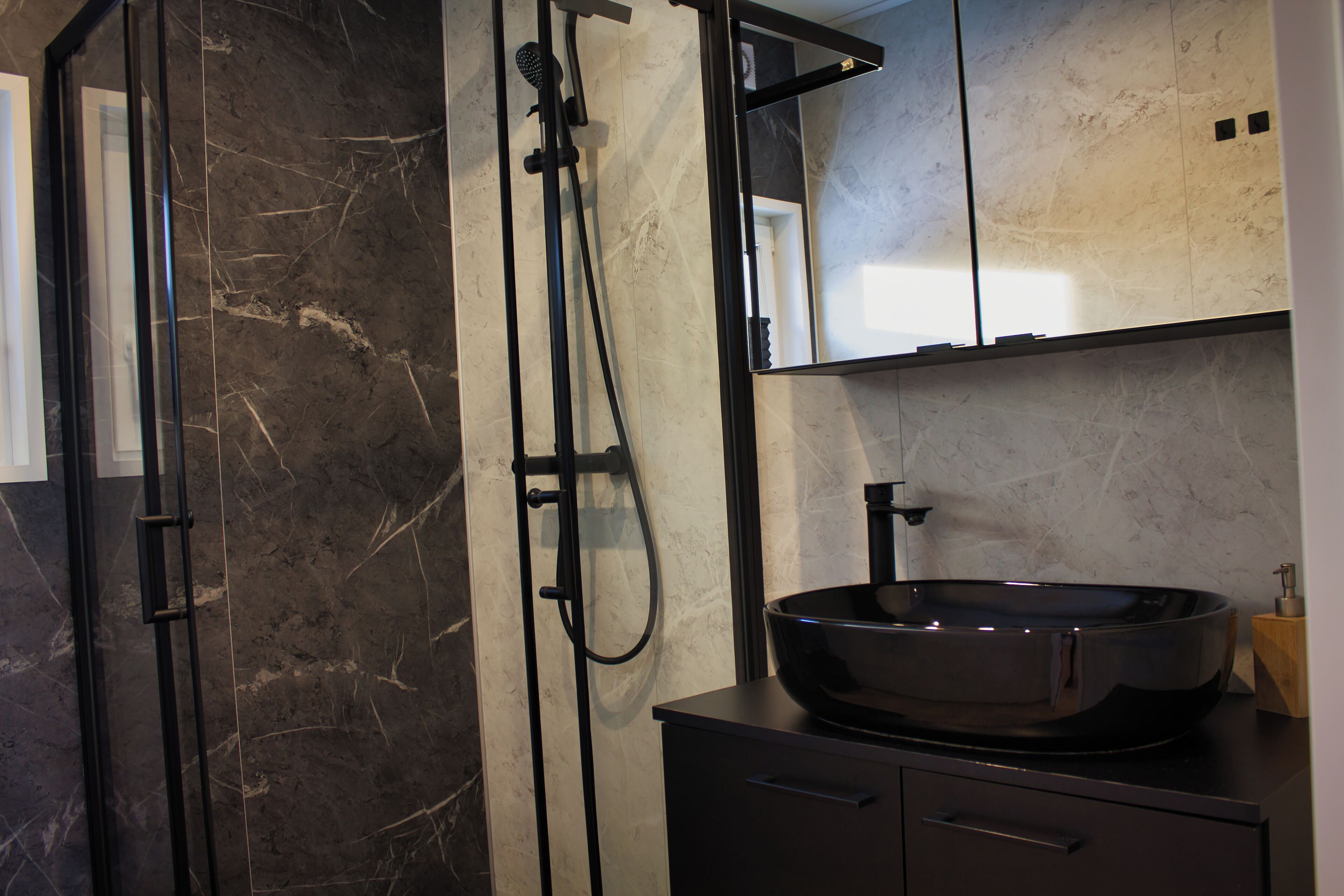 Une salle de bain moderne avec une douche à l’italienne aux parois en marbre noir, un lavabo noir doté d’une grande cuve et un miroir au-dessus du lavabo.