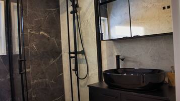 Une salle de bain moderne avec une douche à l’italienne aux parois en marbre noir, un lavabo noir doté d’une grande cuve et un miroir au-dessus du lavabo.