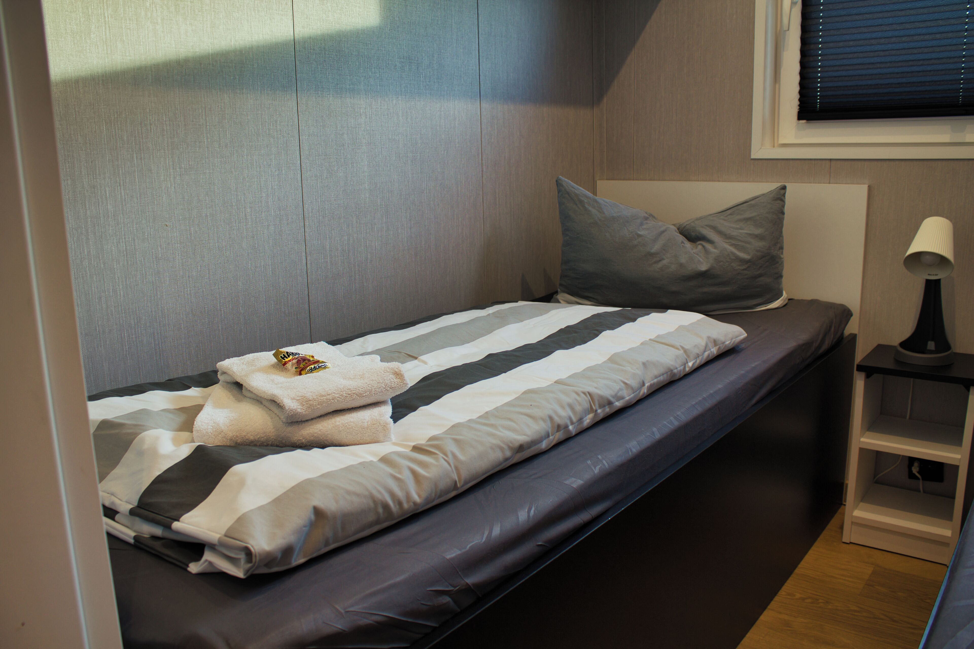 A compact bed with a striped bedspread, a pillow, and a folded towel.