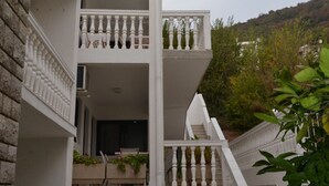 A multi-story building with a balcony on the second floor, a staircase leading to the third floor, and a view of a hillside with trees. - Guest House 4M Gregović - Triple bed Studio 4 (Petrovac na Moru)