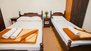 A hotel room with two beds, each with a wooden headboard, white linens, and towels. There is a small table with a vase of flowers between the beds. - Guest House 4M Gregović - Triple bed Studio 4 (Petrovac na Moru)