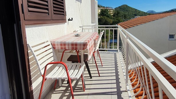 A balcony with a table and chairs, a view of a mountain, and a building with a tiled roof. - Guest House 4M Gregović - Triple bed Studio 4 (Petrovac na Moru)