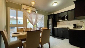 Uma cozinha moderna com armários escuros, uma geladeira de aço inoxidável e um micro-ondas. Há uma área de jantar com uma mesa posta para quatro pessoas, cadeiras e taças de vinho.