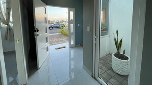 Um corredor com porta que dá para uma área de estacionamento, uma planta em vaso e um candeeiro suspenso.