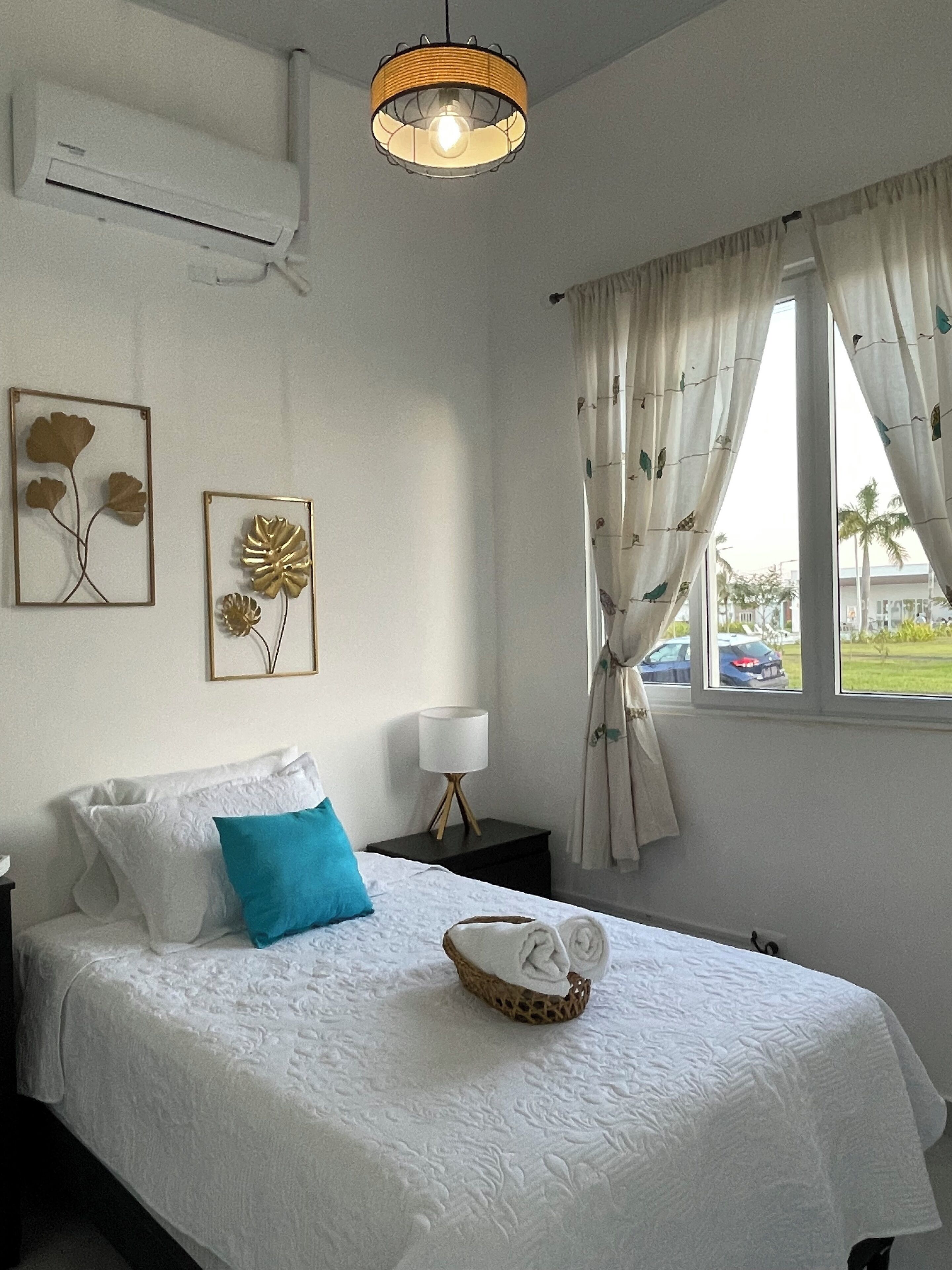 A neatly arranged bedroom with a bed, pillows, a bedside lamp, and wall art.