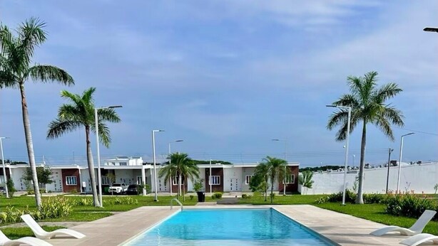 Piscina retangular com água azul cristalina, cercada por palmeiras e espreguiçadeiras.