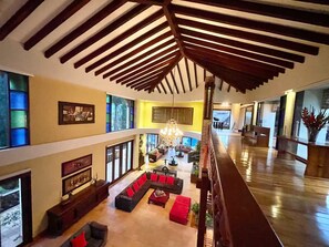 A spacious living area with a high ceiling, a chandelier, and a large window.