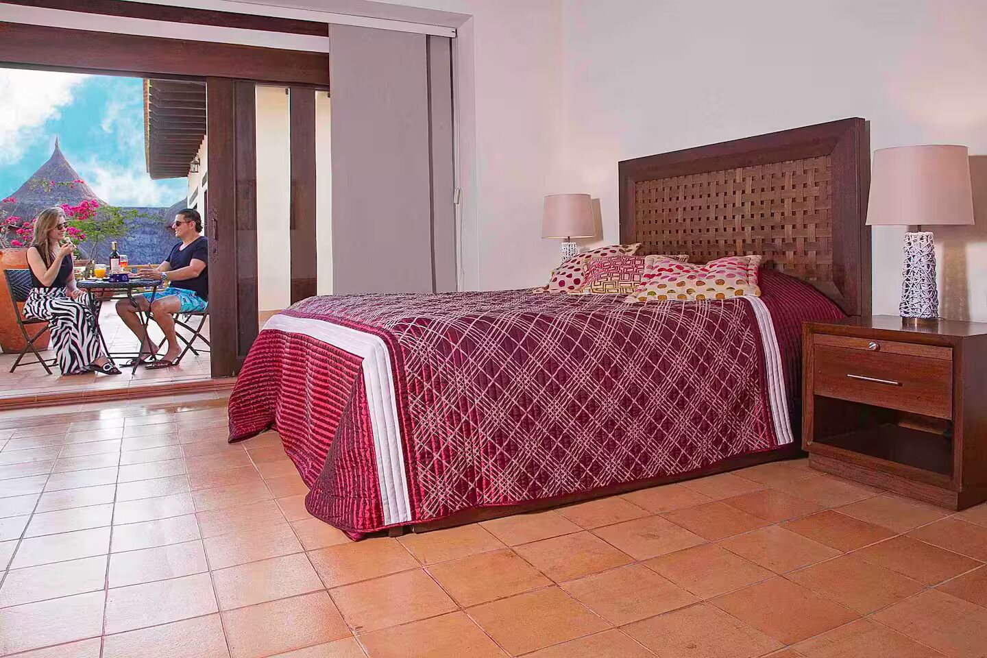 Ein Schlafzimmer mit Bett, Nachttisch und Blick auf einen Essbereich mit zwei Personen.