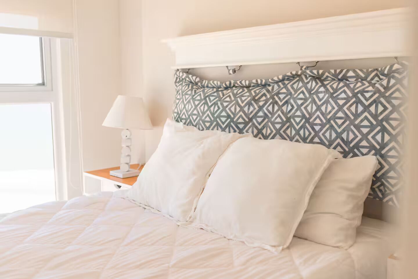 Un letto rifatto con lenzuola bianche, una testiera decorata e un comodino con una lampada.