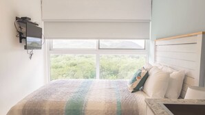 Una camera da letto con una grande finestra, un letto con coperta a righe, una testiera e un comodino.