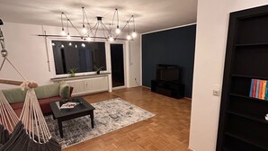 Un salon moderne avec un plancher en bois, un canapé noir, un fauteuil suspendu, une table basse et une bibliothèque.
