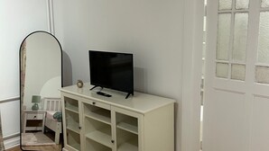 Une pièce avec un meuble blanc, une télévision, un miroir, un lit et une porte.
