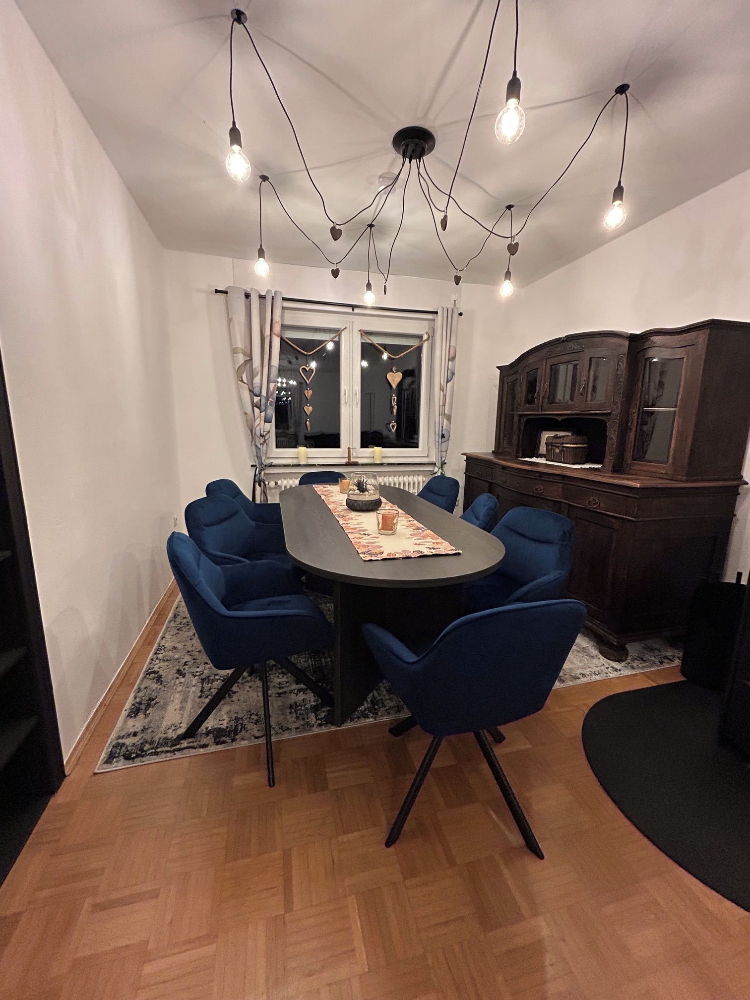 A dining area with a round table, blue chairs, and a chandelier.