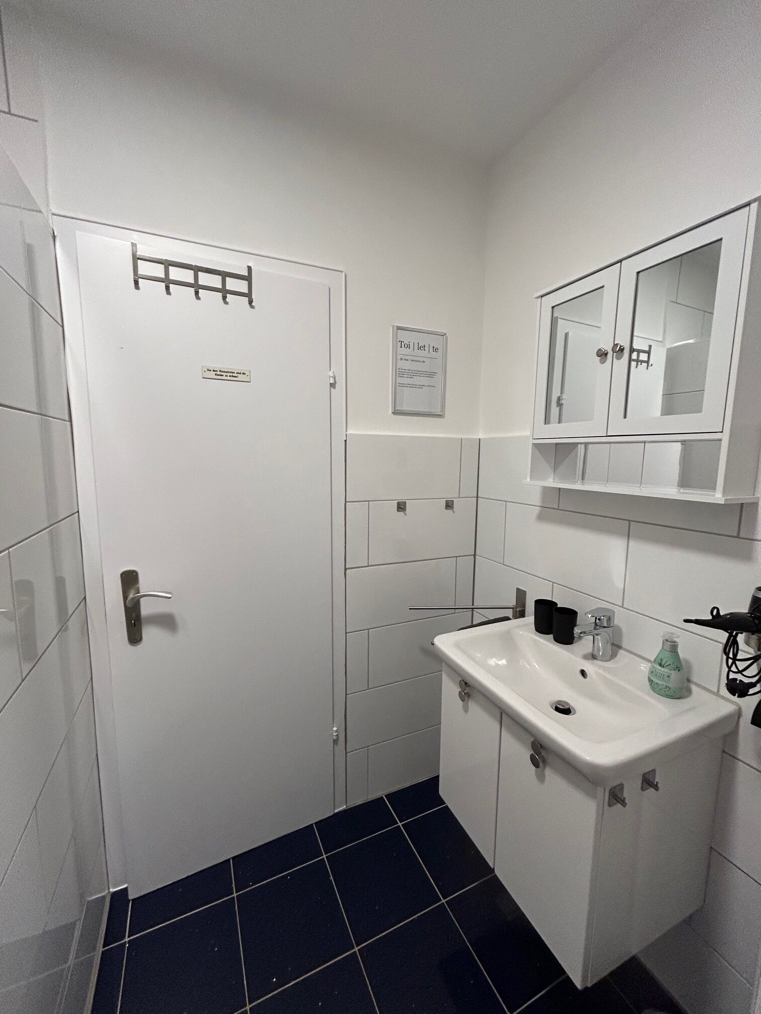 A bathroom with a white door, a sink with a mirror above it, and a black tiled floor.
