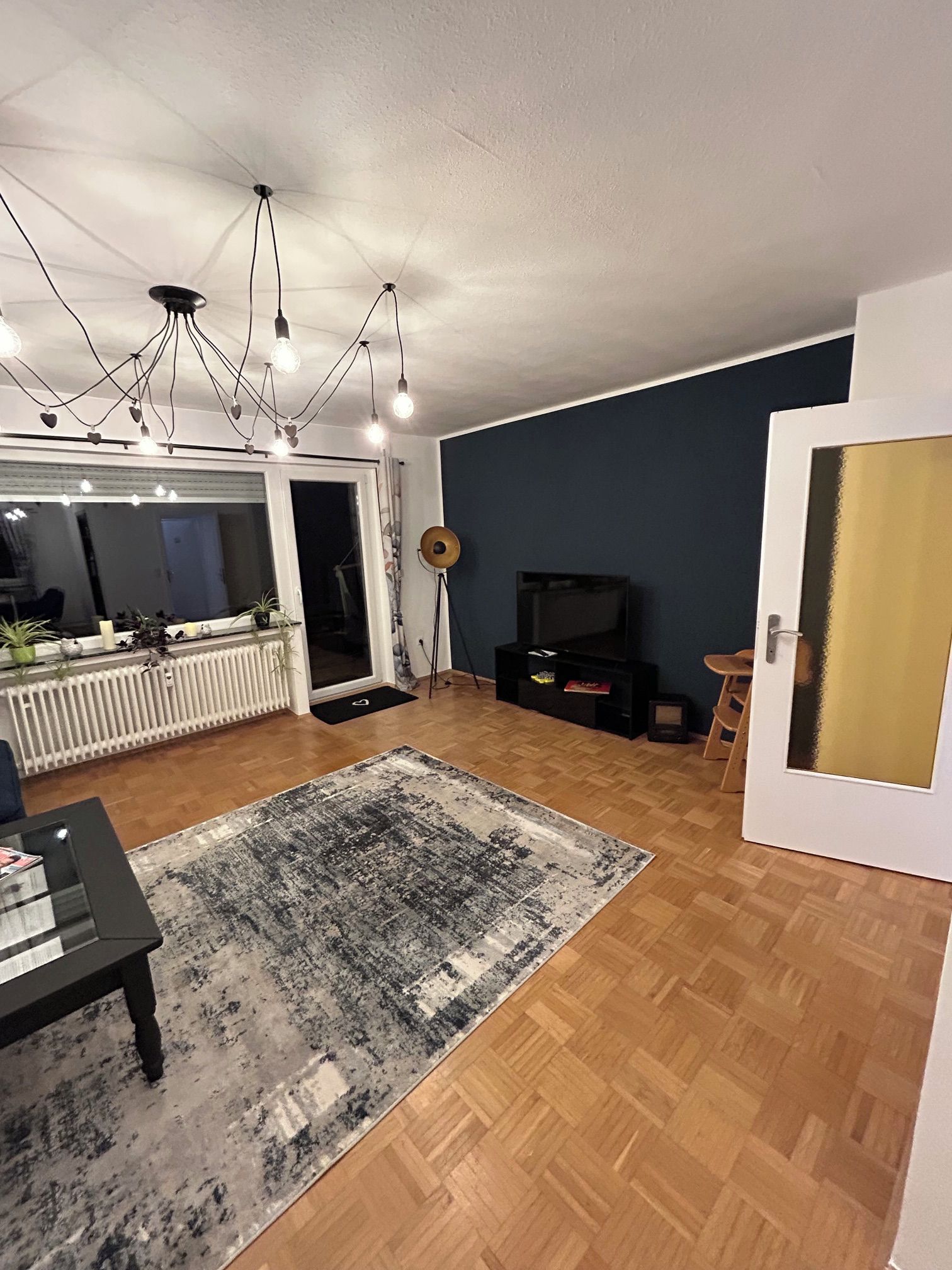 Ett vardagsrum med trägolv, en svart soffa, ett soffbord, en tv och en taklampa.