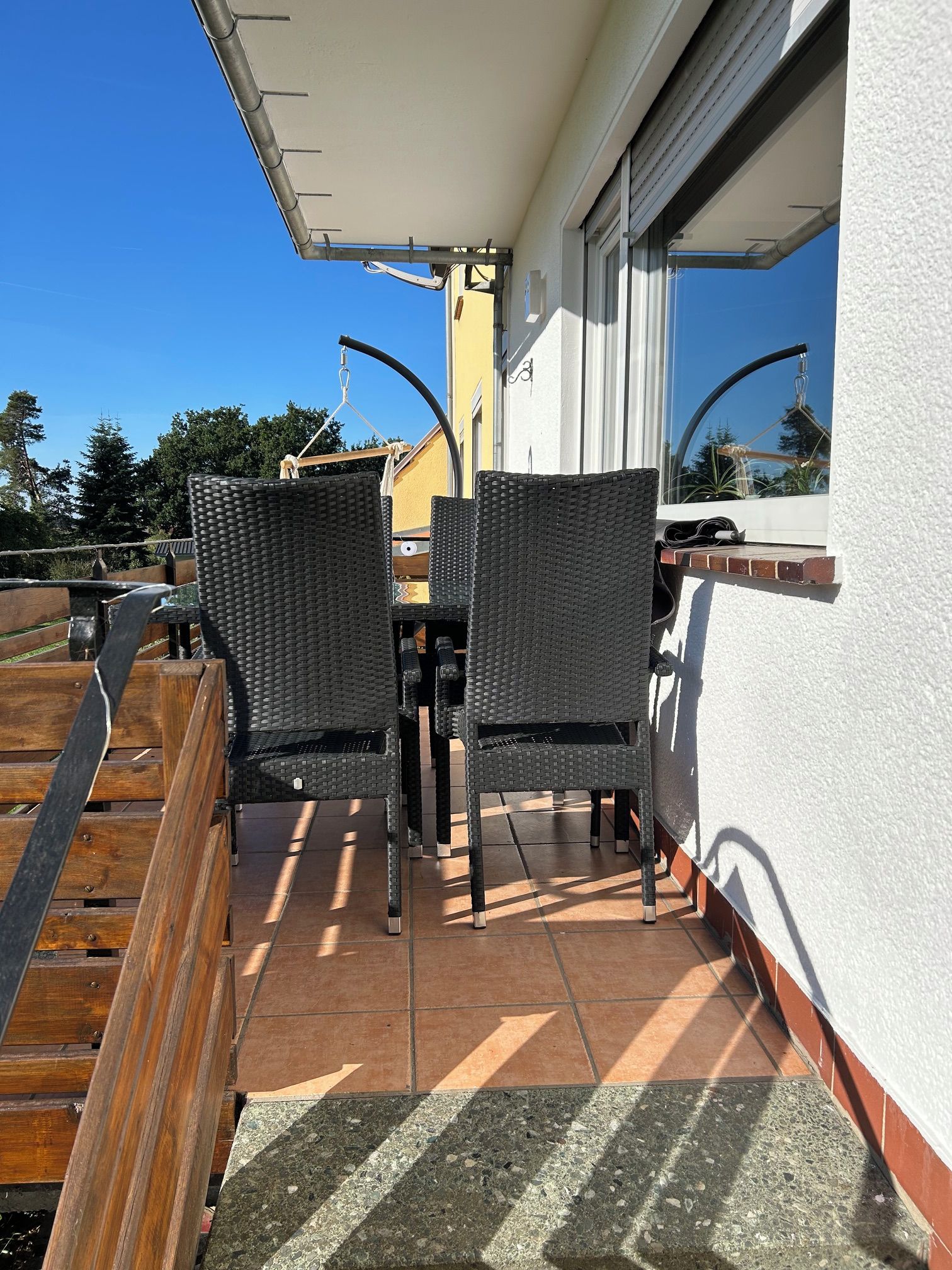 Eine Terrasse mit zwei Korbstühlen und einem Tisch, ein Holzdeck und Blick auf Himmel und Bäume.