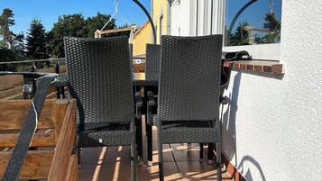 Eine Terrasse mit zwei Korbstühlen und einem Tisch, ein Holzdeck und Blick auf Himmel und Bäume.