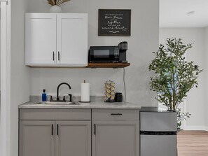 A kitchen with white cabinets, a microwave, a sink, and a potted plant.