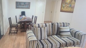 Een woonkamer met een gestreepte bank, een ronde salontafel, en een eethoek met een tafel en stoelen.