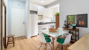 A modern kitchen with white cabinets, a microwave, and a coffee machine. There is a dining area with a glass table and white chairs. - 1-br APT w/ Bbq, 800m From the Sea Dfc0101 (Florianópolis)