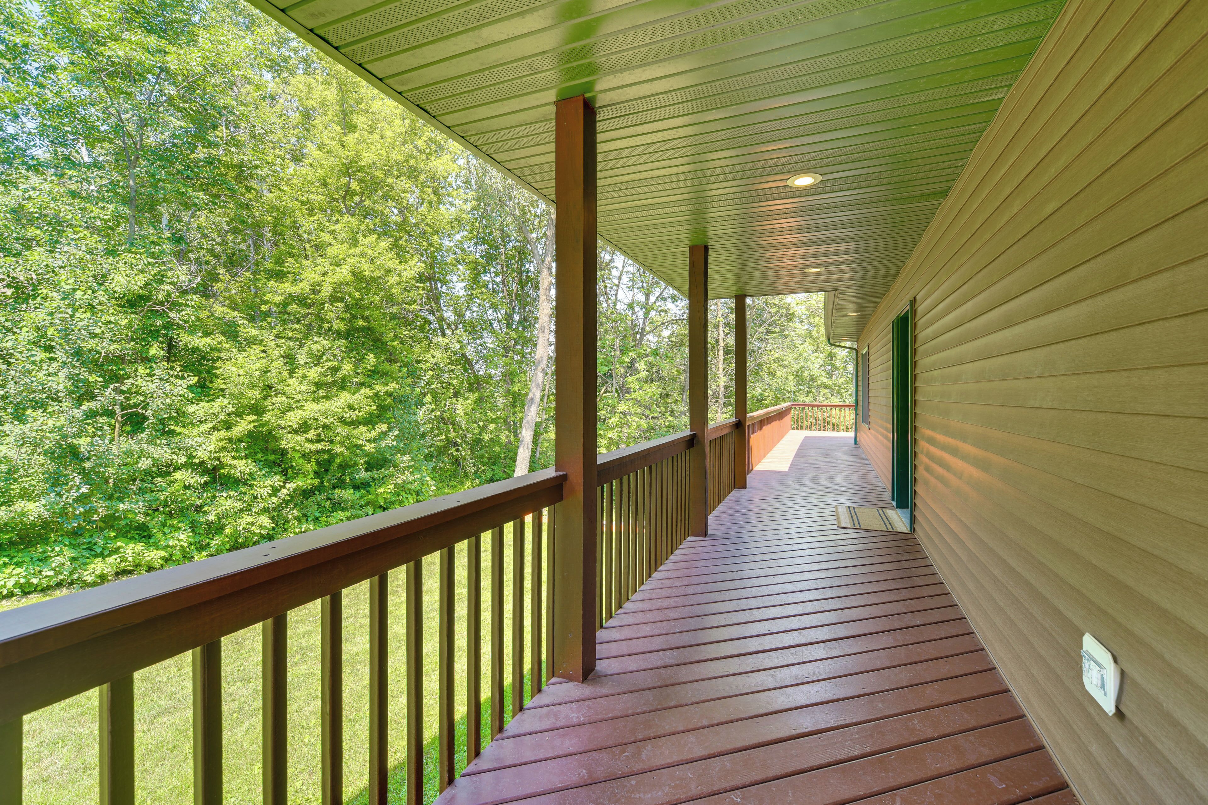 A covered wooden deck with a railing, leading to a covered area with a view of a forest.
