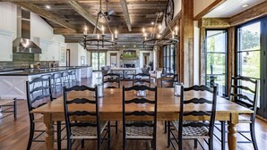 Un comedor amplio con una gran mesa y sillas de madera, una cocina con armarios blancos y ventanas grandes que ofrecen vistas al exterior.