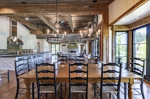Un comedor amplio con una gran mesa y sillas de madera, una cocina con armarios blancos y ventanas grandes que ofrecen vistas al exterior.