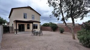 Ein zweistöckiges Haus mit überdachter Terrasse, einem eingezäunten Garten und einem Baum.