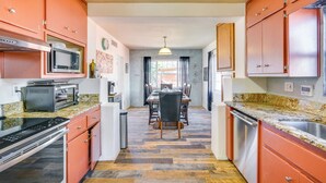 A kitchen with orange cabinets, a microwave, a toaster, and a dining area with a table and chairs. - Fire Pits & Grill at Central Tucson Home Base! (Tucson)
