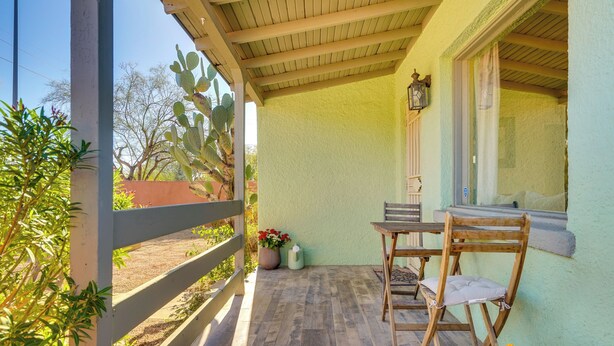 A covered patio with a wooden table and chairs, a potted plant, and a window with a curtain. - Fire Pits & Grill at Central Tucson Home Base! (Tucson)