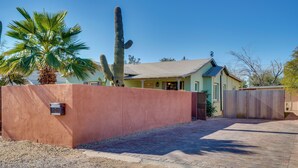 Una casa con entrada pavimentada, cerca de madera y un cactus grande en el jardín.