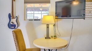 Una habitación con televisor, guitarra, lámpara y una silla.