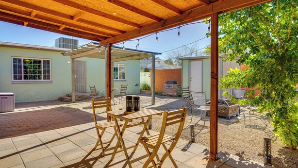 Un patio al aire libre con mesas y sillas de madera, una zona de estar cubierta y vistas a un barrio residencial.