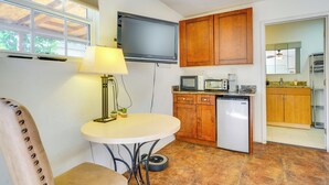 Una cocina compacta con televisión integrada, armarios de madera, un refrigerador pequeño y una mesa de comedor con lámpara.