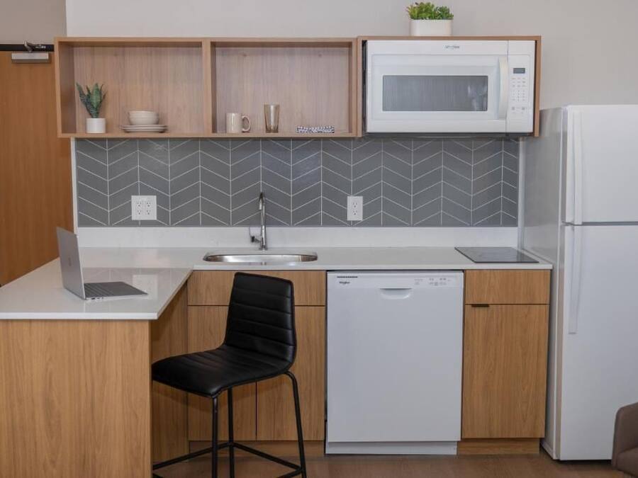 Una cocina compacta con microondas, lavavajillas y un pequeño comedor con una silla.