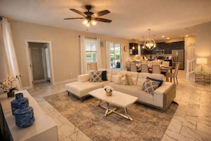 A modern living room with a sofa, coffee table, and a ceiling fan. - The Grand Retreat at ChampionsGate w/pool (Four Corners)