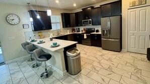 Una cocina moderna con armarios oscuros, electrodomésticos de acero inoxidable, suelo de baldosas de mármol y un reloj en la pared.