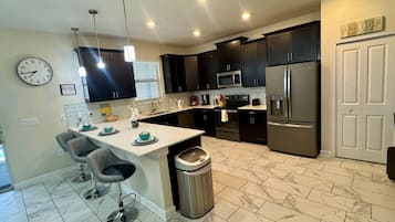 A modern kitchen with dark cabinets, stainless steel appliances, a marble-tiled floor, and a clock on the wall.