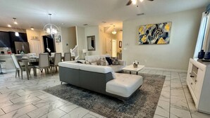 Una sala de estar moderna con un sofá gris, una mesita blanca y una zona de comedor con sillas.