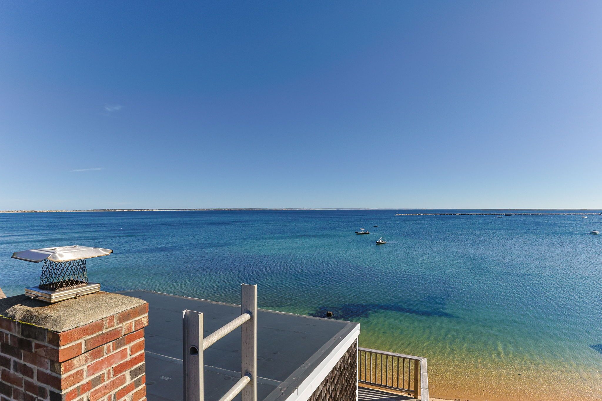 A clear view of a beach with calm waters, a distant pier, and a brick structure with a chimney.