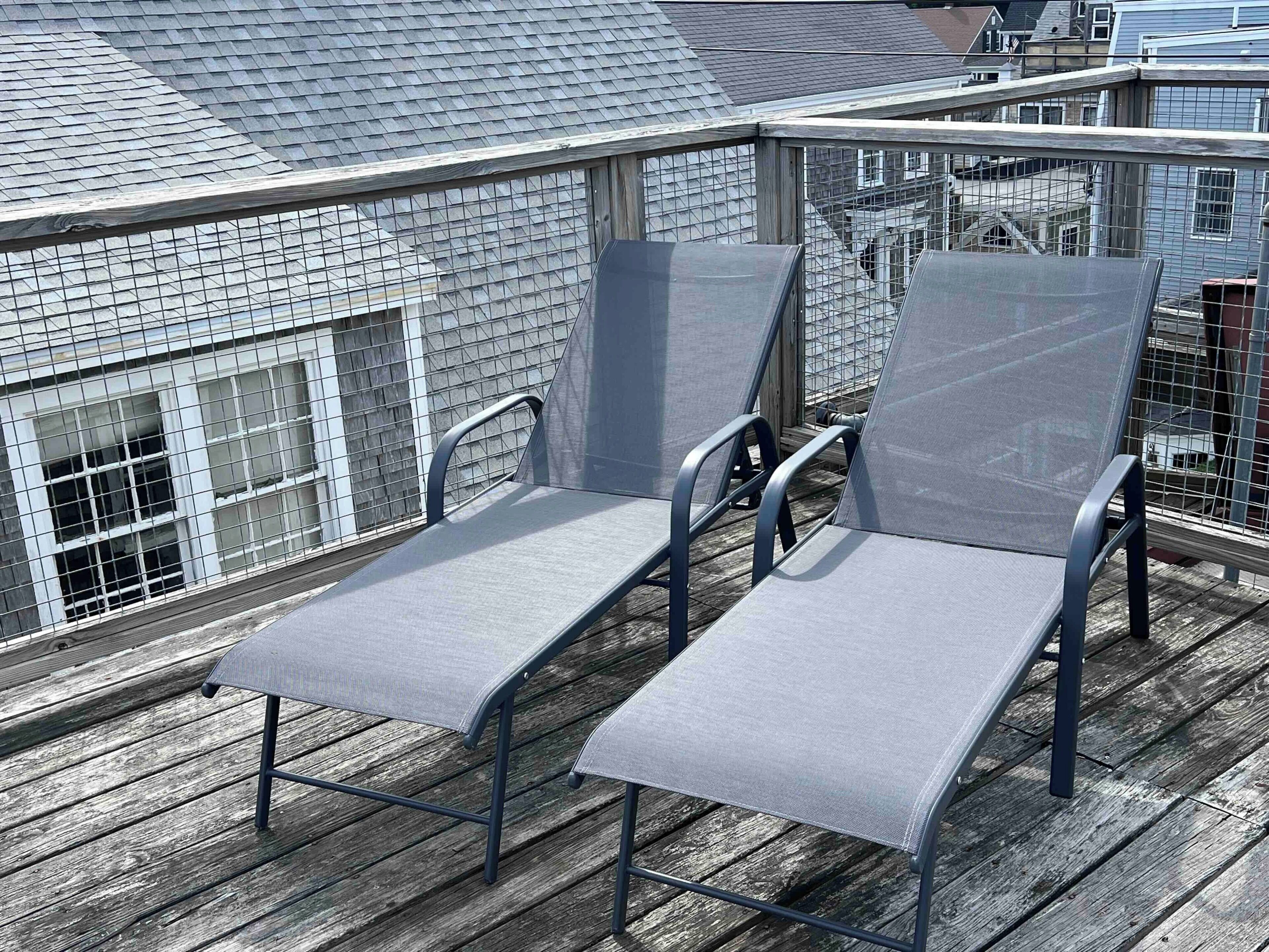 A rooftop deck with two lounge chairs and a metal railing.
