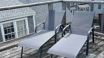 A rooftop deck with two lounge chairs and a metal railing.