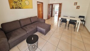 A living room with a sectional sofa, a round coffee table, and a dining area with a table and chairs. - Belsol House (Altura)