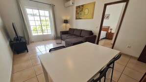 A modern living room with a white dining table, a sofa, a lamp, and a TV. - Belsol House (Altura)